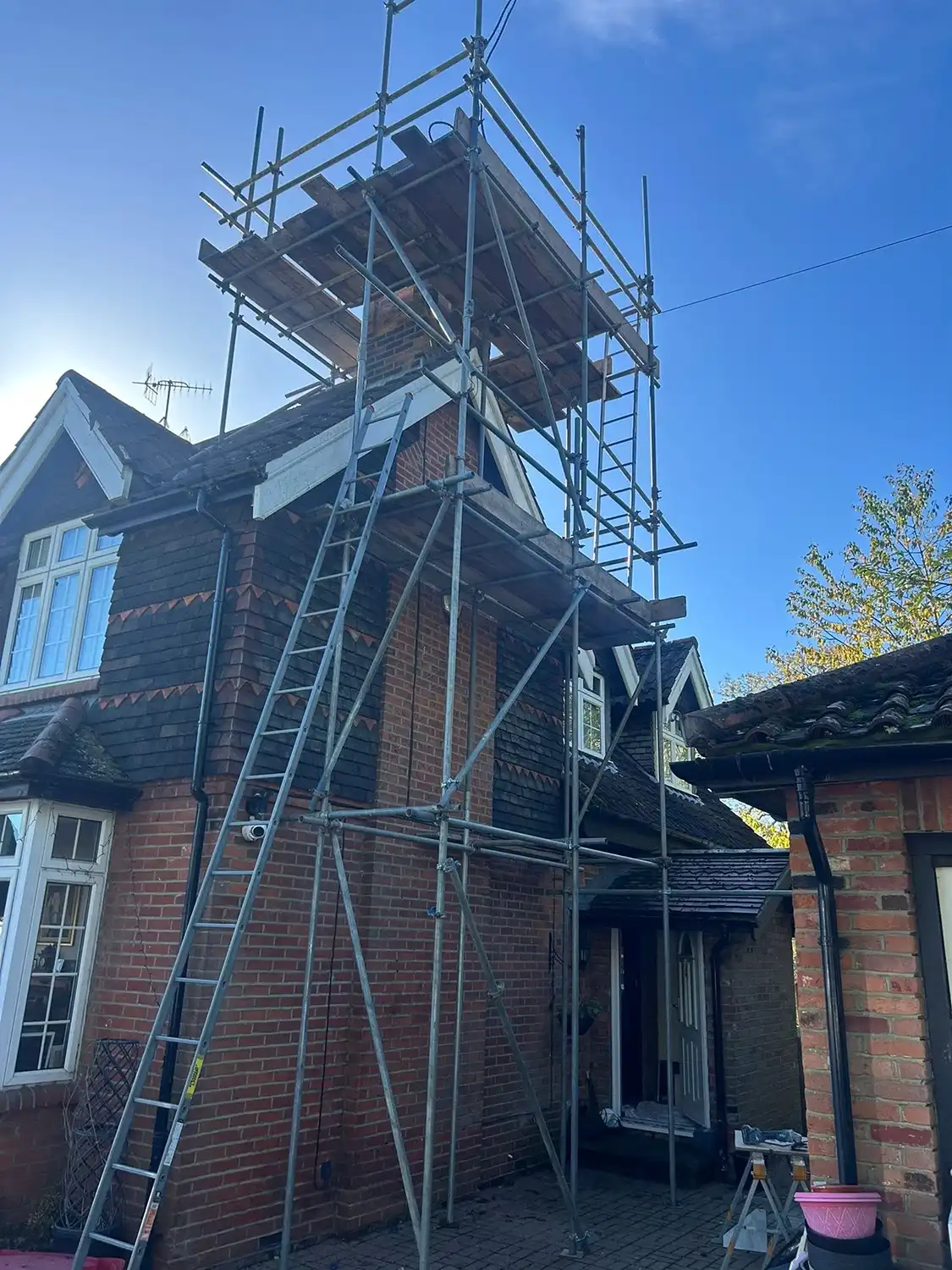 House chimney under repair with metal scaffolding and ladders against a clear blue sky.