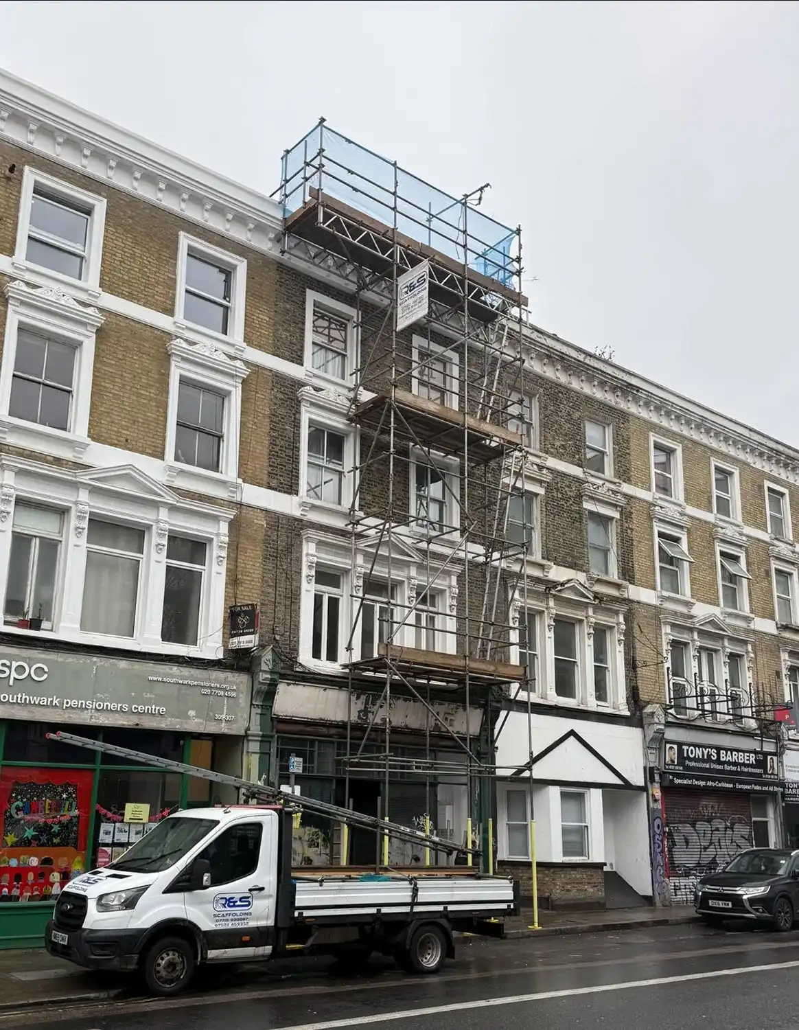 Scaffolding erected on front of a brick building with a white truck parked on the street in front.