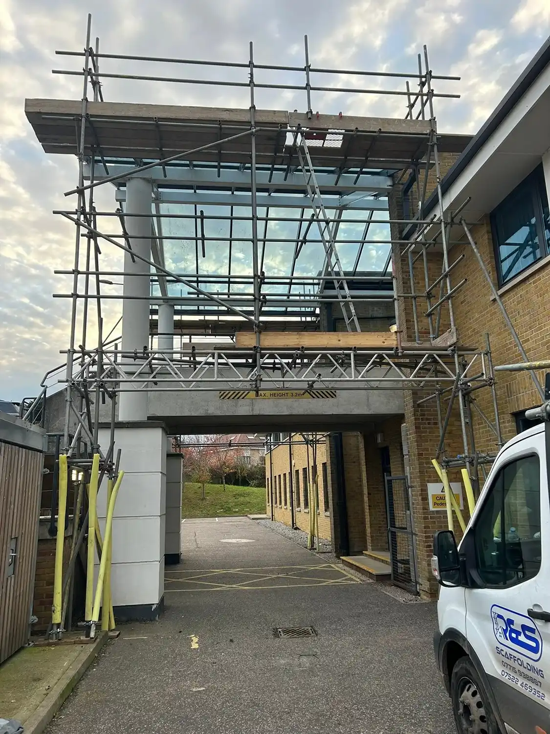 Construction scaffolding on a building entrance with a white van parked nearby on a cloudy day.