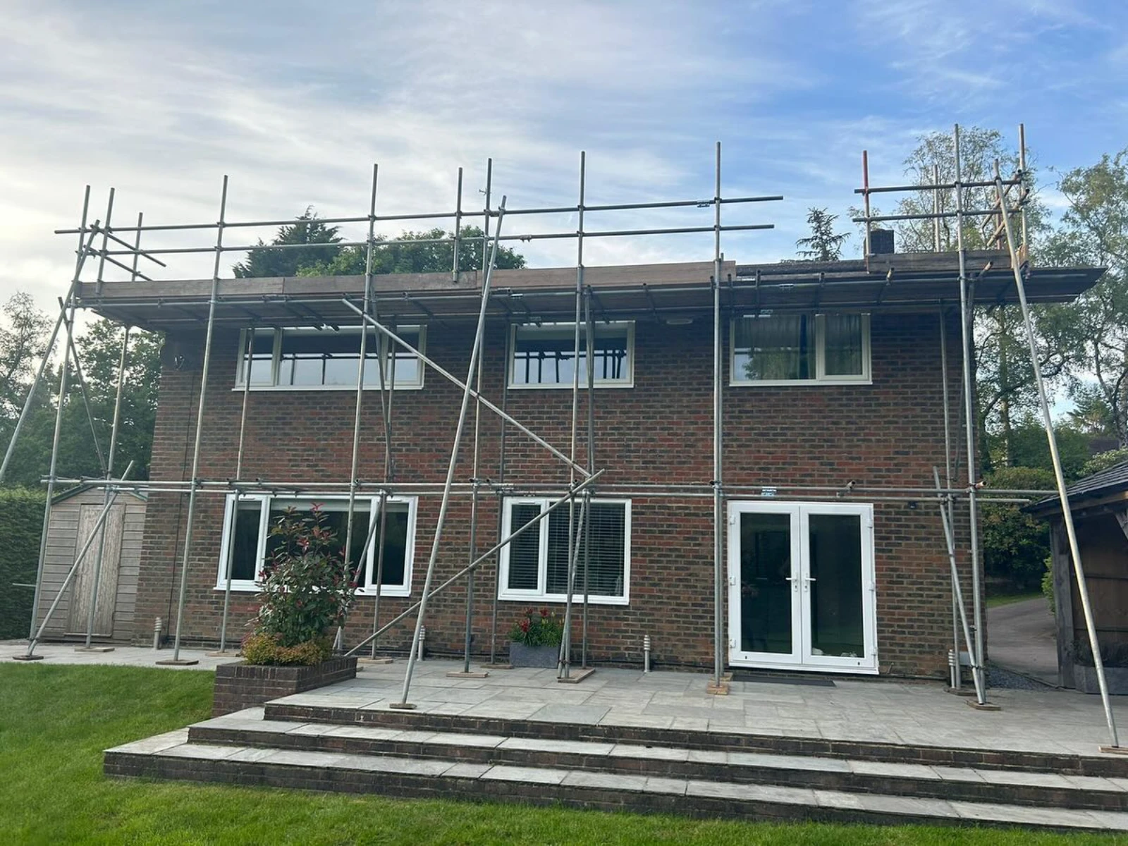 Two-story brick house with scaffolding around it and a small garden in front.