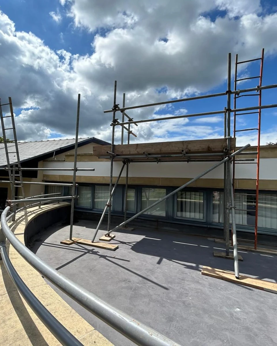 Scaffolding set up on a curved rooftop terrace under a cloudy blue sky.