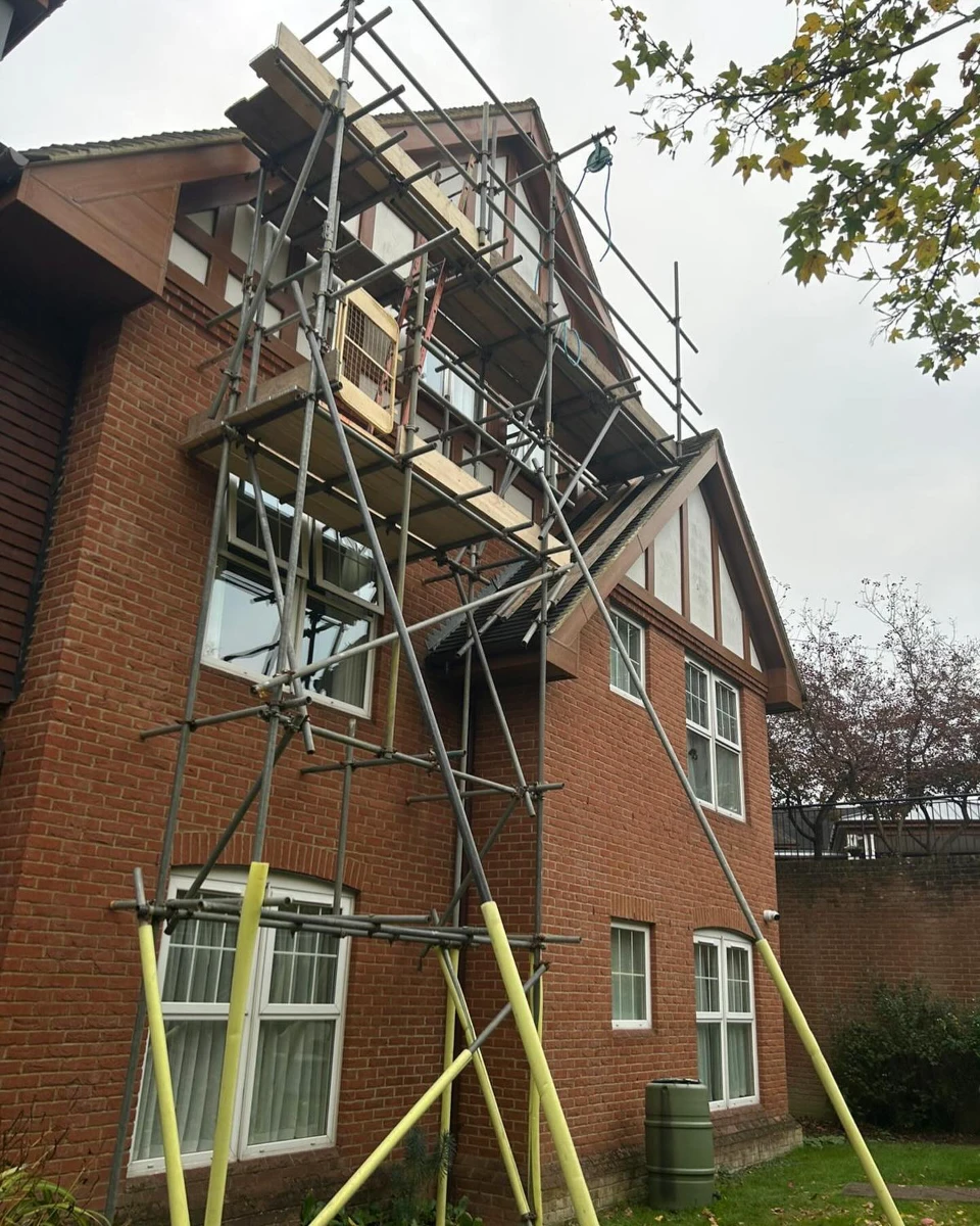 Scaffolding erected against a two-story brick house with white-trim windows and a tiled roof.
