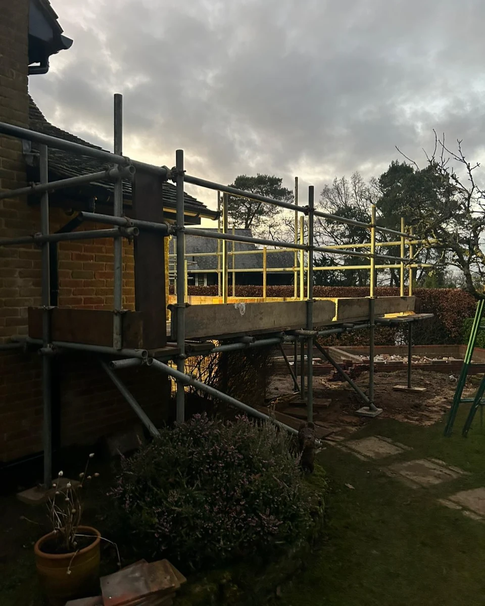 Metal scaffolding with wooden platforms set up next to a brick house under cloudy sky.