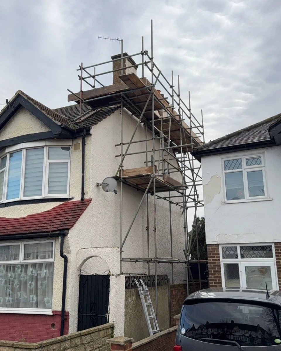 Scaffolding erected on the side of a two-story house with a car parked in front.