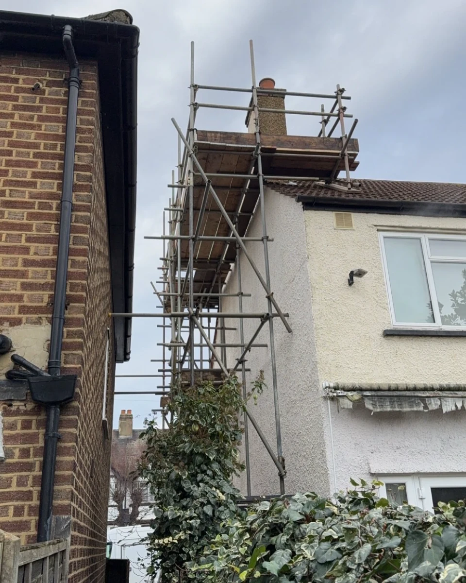 Metal scaffolding built around the side of a residential house for exterior work near the chimney.