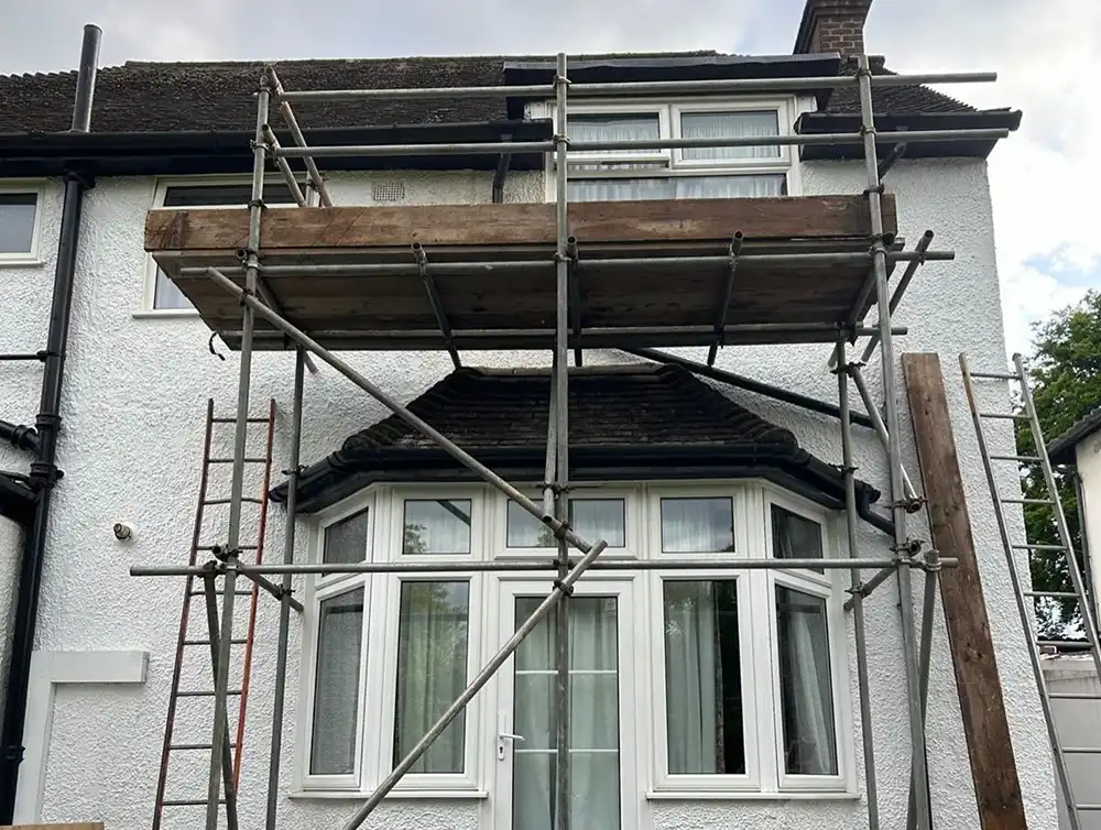 Metal scaffolding with wooden planks set up in front of a two-story white house with bay windows.